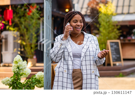 Plus size woman smiling while talking on mobile phone walking outdoors Plus size woman smiling while talking on mobile phone walking outdoors 130611147