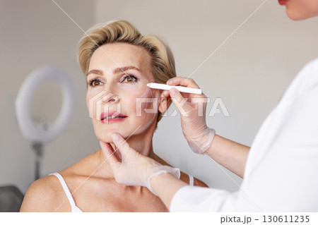 Closeup of mature woman with face contour lines during anti-aging consultation at beauty clinic. Dermatologist preparing for cosmetic facelift procedure. Skincare, rejuvenation and aesthetic treatment Closeup of mature woman with face contour lines during anti-aging consultation at beauty clinic. Dermatologist preparing for cosmetic facelift procedure. Skincare, rejuvenation and aesthetic treatment 130611235