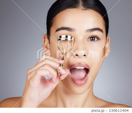 Wow, face and woman with eyelash curler in studio isolated on a gray background. Portrait, makeup surprise and cosmetics of female model with tool or product to curl eyelashes for beauty aesthetics. 130611404