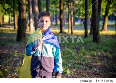 Worried teenager patriot wear blue yellow Ukrainian flag on his shoulders. Spring nature background. Ukraine national symbol. Patriotism 130611650