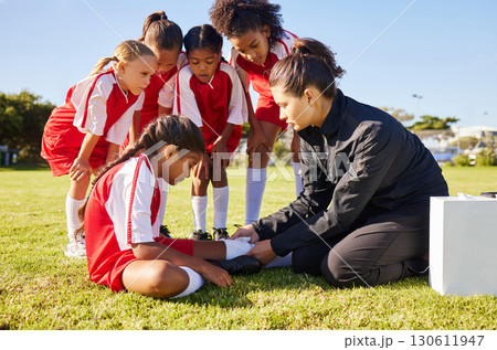 Sports, injury and children soccer team with their coach in a huddle helping a girl athlete. Fitness, training and kid with a sore, pain or muscle sprain after a match on an outdoor football field. Sports, injury and children soccer team with their coach in a huddle helping a girl athlete. Fitness, training and kid with a sore, pain or muscle sprain after a match on an outdoor football field. 130611947