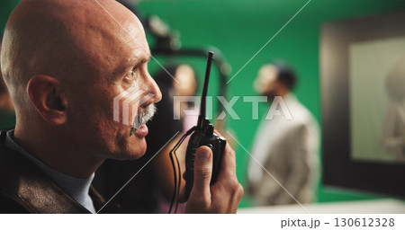 Man, director and radio with green screen for action, scene or instruction in production studio. Male person, producer or manager talking with signal or cut for take, cue or special effects in set Man, director and radio with green screen for action, scene or instruction in production studio. Male person, producer or manager talking with signal or cut for take, cue or special effects in set 130612328