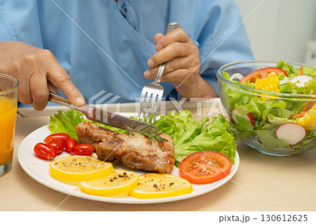 Asian senior woman patient eating pork chop stake and vegetable salad for healthy food in hospital. Asian senior woman patient eating pork chop stake and vegetable salad for healthy food in hospital. 130612625