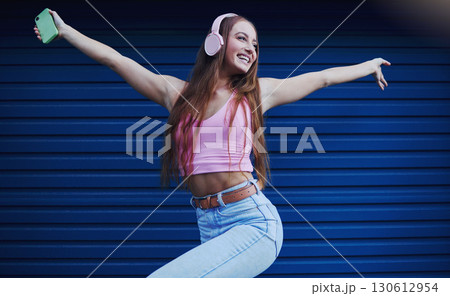 Woman, headphones and dancing outdoor for celebration, achievement and streaming music for fun. Young female, lady or headset for radio, listen to audio or songs with confident girl and casual outfit 130612954