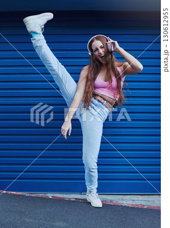 Crazy music, freedom and excited girl on blue background in city listening to track and audio on headphones. Fashion, lifestyle and woman with leg up for dance, happy attitude or streaming song Crazy music, freedom and excited girl on blue background in city listening to track and audio on headphones. Fashion, lifestyle and woman with leg up for dance, happy attitude or streaming song 130612955