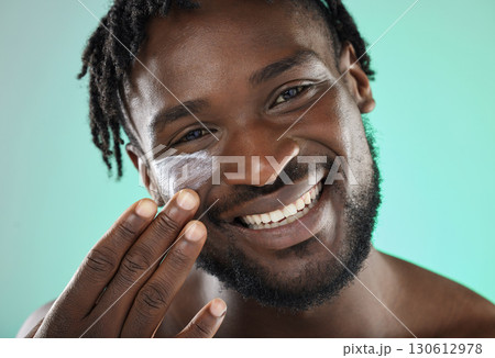 Skincare, face cream and portrait of a black man in a studio with a beauty, health and natural skin routine. Wellness, cosmetic and African guy with facial spf, lotion or creme by a blue background. 130612978