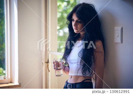 Mental health, depression and sad woman thinking with water, stress and anxiety in a house. Depressed, lonely and goth girl with a drink, emotional and comtemplating problems in the lounge of home 130612991