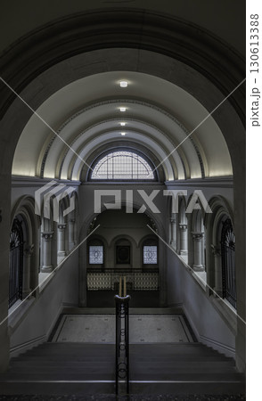 a grand staircase with a prominent wooden handrail leading towards a large arched window at the top, 130613388