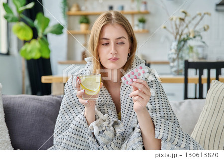 Young woman with fever sick in summer, sitting at home with pills cup of hot tea 130613820