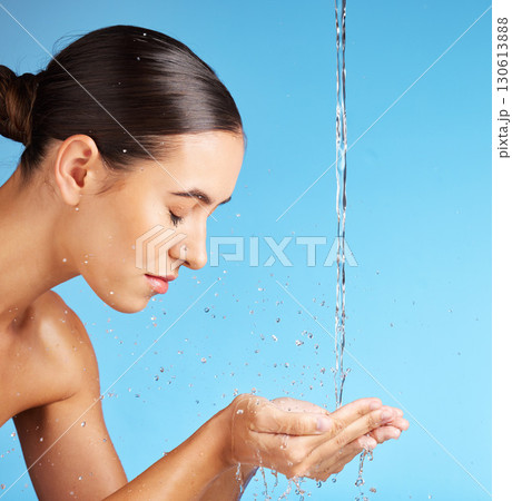 Woman, hands and water for face wash, skincare hydration or hygiene against a blue background. Beautiful female model in facial cleaning, washing or cleansing for skin rehydration or dermatology 130613888