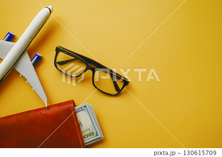 flat lay of airplane model, pocket with money and eyeglasses on yellow background, travel and holidays concept 130615709