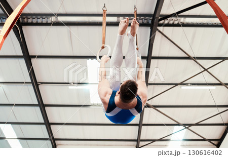 Man, acrobat and gymnastics hanging on rings in fitness for practice, training or workout at gym. Professional male gymnast on ring circles below for athletics, acrobatics or strength exercise 130616402