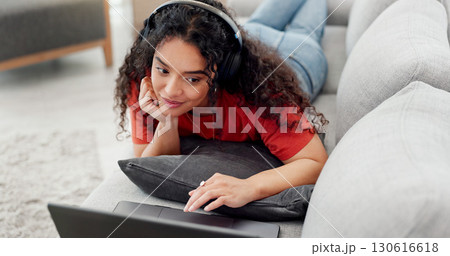 Headphones, laptop and subscription with woman on sofa in living room of home for watching online. Computer, relax and video streaming with person in apartment for break, entertainment or media 130616618