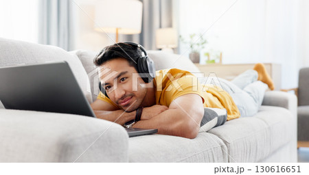 Man, laptop and headphones on sofa for break, social media and video streaming or website in home. Movie, internet audio and male person on couch with technology, relax and watching film on app 130616651
