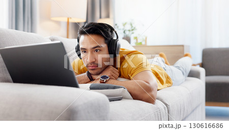 Man, laptop and headphones on sofa for movie, social media and video streaming or website in home. Relax, internet audio and male person on couch with technology, break and watching film on app 130616686