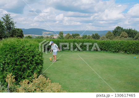 Young child explores the lush garden, engaging with the landscape on a sunny day. Surrounded by greenery and open sky, the scene captures playful outdoor exploration and nature appreciation. Young child explores the lush garden, engaging with the landscape on a sunny day. Surrounded by greenery and open sky, the scene captures playful outdoor exploration and nature appreciation. 130617465