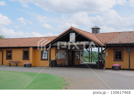 Wooden golf clubhouse with tiled roof, entrance signs to driving range, practice hall and golf simulator. Cozy building surrounded by nature, ideal for sports promotion, events, leisure and tourism. Wooden golf clubhouse with tiled roof, entrance signs to driving range, practice hall and golf simulator. Cozy building surrounded by nature, ideal for sports promotion, events, leisure and tourism. 130617468