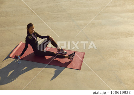 Beautiful young woman relaxing on yoga mat after active outdoor fitness workout in city 130619928
