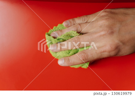 Top view of housewife male hand cleaning red shelf with rag and detergent, ensuring spotless and dust-free surface in cleaning routine, close-up. Concept of domestic work, housekeeping and household. Top view of housewife male hand cleaning red shelf with rag and detergent, ensuring spotless and dust-free surface in cleaning routine, close-up. Concept of domestic work, housekeeping and household. 130619979