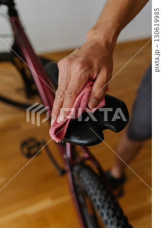 Cyclist male cleaning saddle of bicycle with microfiber cloth, performing detailed maintenance after trail riding, close-up. Concept of repair and maintenance of bicycle transport. 130619985