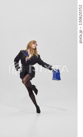 Woman posing dynamically in black blazer and tights holding blue bag 130620352