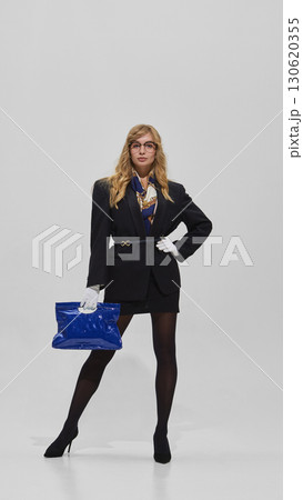 Woman in glasses and dark blazer with gloves holding blue bag in bold pose 130620355
