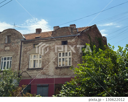 Old brick house in Belgrade with tiled roof, weathered facade and greenery in front under summer sky. Architectural heritage, urban tradition, history, nostalgia, society, cultural identity and 130622012
