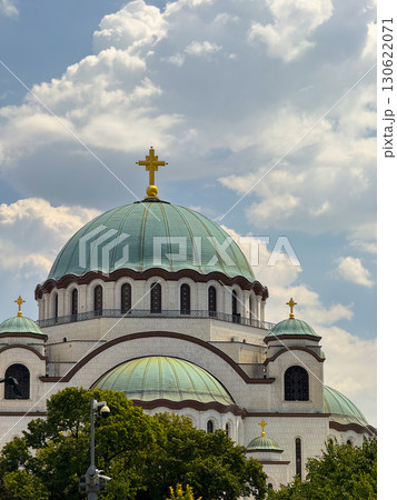 Saint Sava temple dome with golden crosses under clouds in Belgrade Serbia surrounded by trees. Religious architecture, Christian orthodoxy, cultural landmark, faith, tradition, history and spiritual 130622071