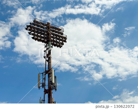 Tall floodlight tower with antennas and lamps at Belgrade stadium under partly cloudy sky. Urban infrastructure, sports facility, communication technology, power installation and modern engineering in Tall floodlight tower with antennas and lamps at Belgrade stadium under partly cloudy sky. Urban infrastructure, sports facility, communication technology, power installation and modern engineering in 130622072