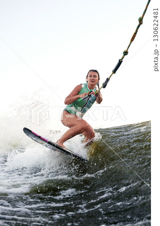 Woman wakeboarding on choppy water holding a rope during a sunny day 130622481