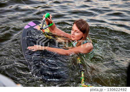 Woman holding a rope on a wakesurf board in water 130622492