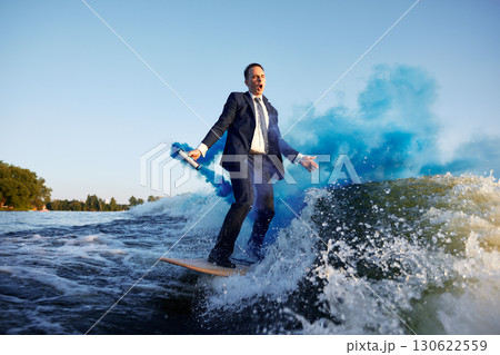 Businessman surfing on water with blue smoke and scenic background 130622559