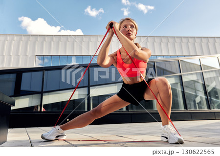 Woman Performing Fitness Exercises Outdoors Using Resistance Bands 130622565