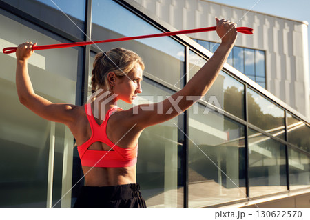 Athletic woman exercising outdoors with resistance band under bright sunlight 130622570