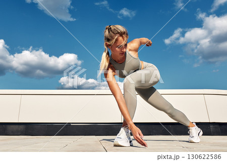 Woman performing fitness stretches outdoors under a sunny sky 130622586