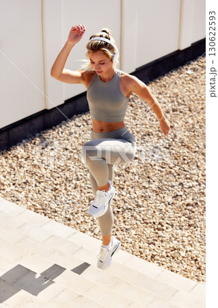 Woman exercising outdoors in sportswear, performing stairs workout under sunlight Woman exercising outdoors in sportswear, performing stairs workout under sunlight 130622593