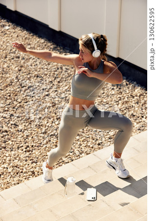 Active woman exercising outdoors with headphones and fitness gear, promoting healthy lifestyle 130622595