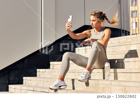 Woman taking selfie after workout on urban stairs in sunlight 130622602