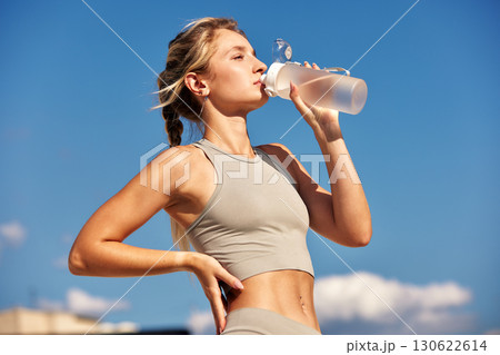Young woman drinking water outdoors on a sunny day for hydration 130622614