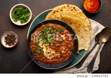 Traditional Indian Punjabi dish Dal makhani with lentils and beans in black bowl served with naan flat bread, fresh cilantro and two spoons on brown concrete rustic table top view Traditional Indian Punjabi dish Dal makhani with lentils and beans in black bowl served with naan flat bread, fresh cilantro and two spoons on brown concrete rustic table top view 130622783