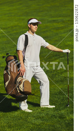 Golfer standing on field with golf bag and club in sunlight Golfer standing on field with golf bag and club in sunlight 130622872