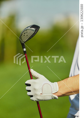 Vertical close up of golfer hand in glove holding club against blurred green background Vertical close up of golfer hand in glove holding club against blurred green background 130622880