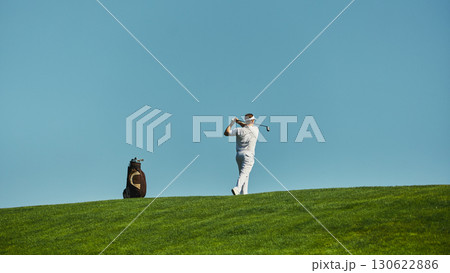 Golfer swinging club on green fairway under clear sky 130622886