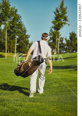 Golfer walking with golf bag across fairway in sunlight Golfer walking with golf bag across fairway in sunlight 130622907