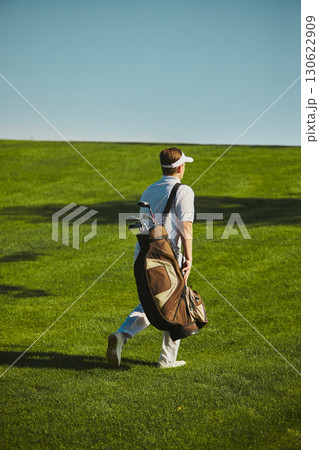 Golfer carrying bag walking across fairway on sunny day Golfer carrying bag walking across fairway on sunny day 130622909