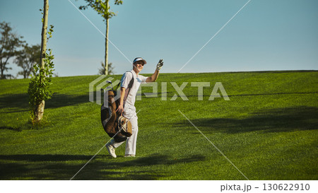 Smiling golfer waving with golf bag on green field Smiling golfer waving with golf bag on green field 130622910