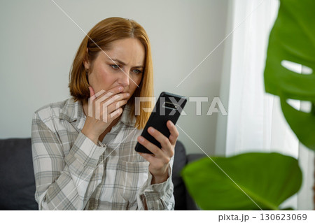 Upset unhappy woman on sofa reading bad news online from her smart phone, home interior Upset unhappy woman on sofa reading bad news online from her smart phone, home interior 130623069