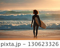 Beautiful young woman with surfboard standing on seashore with waves against sunset background 130623326