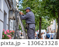Electrician in uniform restoring power by repairing the wiring system while standing on  stepladder on busy city street 130623328