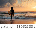 Female surfer standing on the shore of calm sea with surfboard at sunset 130623331